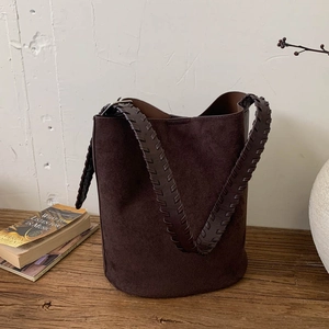 Detail of hand-woven edges on a wide shoulder strap of a brown suede bucket tote bag