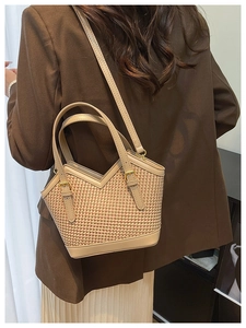 Detail of woven straw tote bag with beige leather trim worn by a model in soft lighting