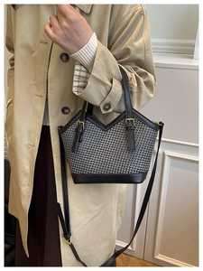 Detail of a chic woven tote bag with black leather trim worn with a khaki trench coat