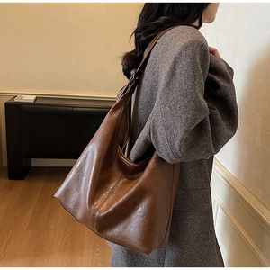 Close-up of a large brown faux leather tote bag worn by a model in a minimalist room