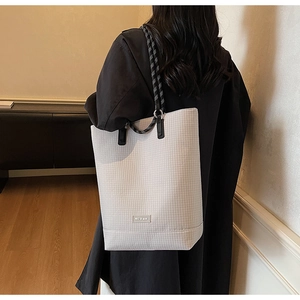 Detail view of small plaid canvas bucket tote bag with rope handle worn on shoulder
