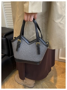 Detail of tweed woven tote bag featuring black leather trim and gold buckle side accents