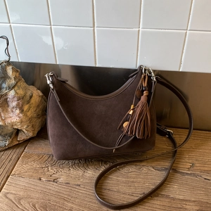 Detail of dark brown suede crescent bag featuring vintage fringe and bead charm on wood