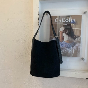 Close-up of black suede bucket bag with woven shoulder strap and metal buckle detail