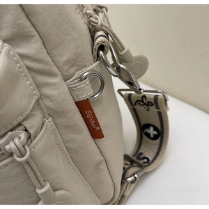 Détail du sac bandoulière en nylon beige avec étiquette orange et sangle à motifs