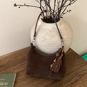 Detail of dark brown suede hobo bag with bohemian tassel and beaded charm on wooden surface