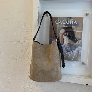 Detail of khaki suede bucket bag with decorative dark brown braided rope shoulder strap