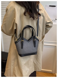 Detail of minimalist black woven tote bag with V-cut leather trim and gold buckle