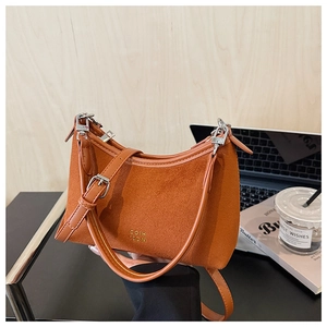Detail der karamellfarbenen Wildledertasche mit Goldbuchstaben neben Laptop und Kaffee