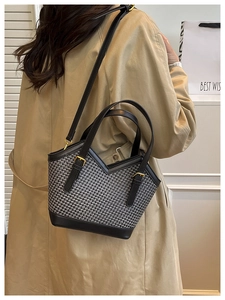 Detail of woven tote bag with black leather trim and adjustable shoulder strap on model