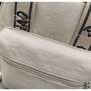 Détail du sac bandoulière en nylon beige montrant la poche zippée et la couture