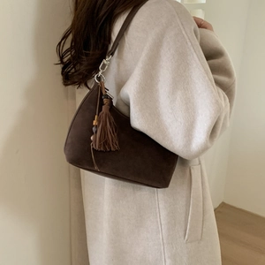 Close-up of deep brown suede hobo bag with tassel detail worn with a wool coat