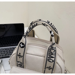 Détail du sac en nylon crème avec des sangles tissées lettrées et plusieurs compartiments
