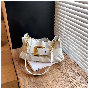 Detail of white pleated shoulder bag with gold buckle on a wooden desk with a book