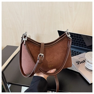 Detail einer braunen Wildleder-Hobo-Tasche mit Lederbesatz und Goldlogo am Tisch