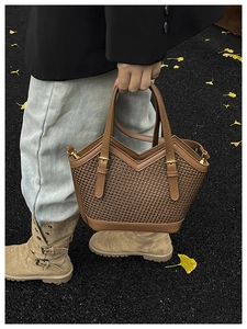Detail of brown woven tote bag with smooth leather handles and gold metal hardware