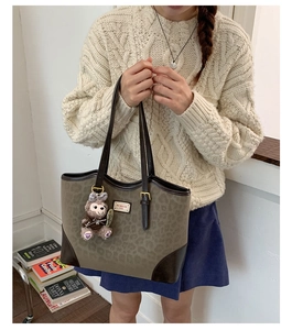 Dettaglio della borsa tote leopardata con bordi in pelle marrone e ciondolo a orso