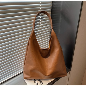 Close-up of brown textured PU leather tote bag featuring a minimalist logo and wide strap