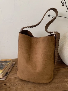 Retro dark brown suede bucket bag with a wide woven shoulder strap on a wooden table