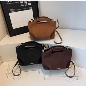 Detail view of suede bucket bags in black, caramel, and wine red with oval cutout handles