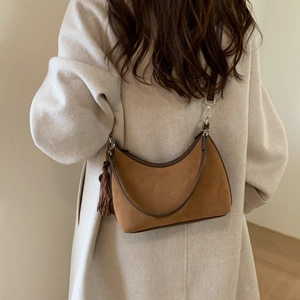 Detail of caramel suede hobo bag with brown leather trim and tassel on a beige coat