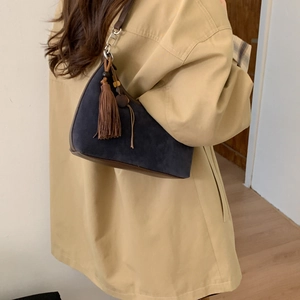 Detail view of navy blue suede dumpling bag with brown leather strap and tassel