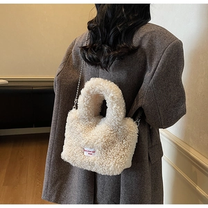 Dettaglio borsa a secchiello beige in pile con tracolla a catena indossata da modella