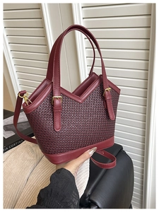 Detail of dark red woven tote bag with gold hardware and elegant textured finish