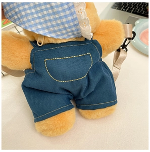 Detailed view of yellow plush bear backpack featuring corduroy overalls and lace hat