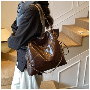 Detail of dark brown quilted tote bag with gold chain strap on a model shoulder