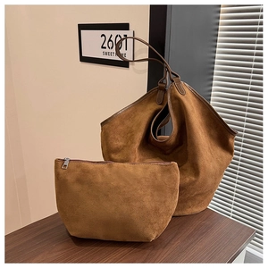 Detail of a brown suede tote bag set with a matching zippered clutch on a wooden surface