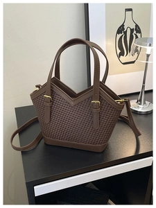 Detail of a brown woven tote bag featuring smooth leather handles and a gold metal buckle