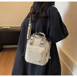 Gros plan du sac bandoulière en nylon beige avec sangles S.JCHAO et poche zippée pratique