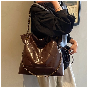 Side view of large brown quilted tote bag with metal chain strap on female model