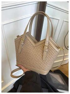 Detail of woven bucket bag featuring beige faux leather trim and golden metal hardware