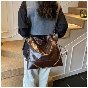 Detail of the large brown quilted tote bag with a golden chain strap on a model