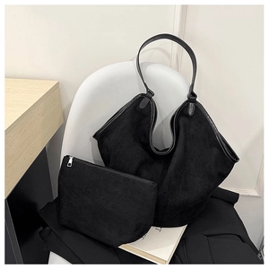 Detail view of black suede tote bag set with matching zippered clutch on white chair