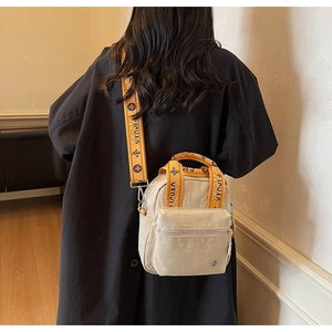 Détail d'un mini sac beige en nylon avec une bandoulière en jacquard jaune à logo