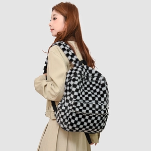 Detail view of the plush black and white checkerboard backpack worn by a model
