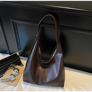 Detail of dark coffee Hobo bag with natural leather texture next to a laptop