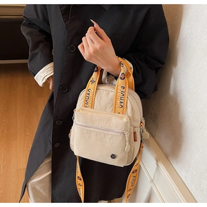 Détail du petit sac carré en nylon beige avec une bandoulière tissée florale orange vif