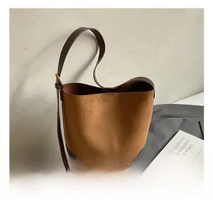 Detail of a brown suede bucket bag with adjustable leather strap on a minimal background