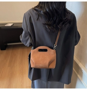 Detail of a brown suede bucket bag featuring a hollow handle and minimalist brand logo