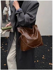 Detail of a large brown quilted tote bag featuring golden chain straps and side drawstrings
