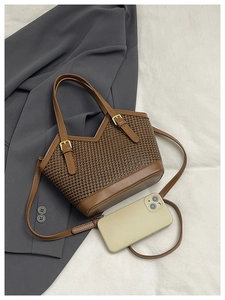 Detail of a brown woven tote bag with leather straps and a V-shaped top opening