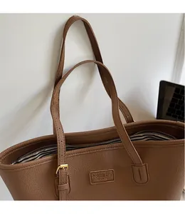Detail of brown litchi pattern leather tote bag showing a metal buckle and fashion logo tag