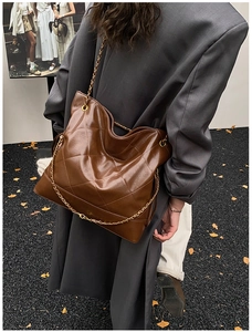 Macro shot of brown quilted leather tote bag with gold chain strap on a model
