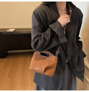 Brown suede crossbody bucket bag with MOEDNT logo shown on model in home setting