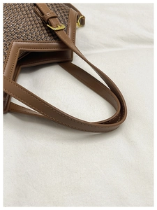 Close-up of woven brown tote bag featuring premium leather handles and gold metal buckles