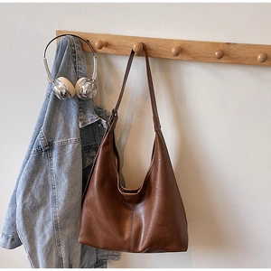 Detailed view of brown leather hobo bag hanging with a denim jacket in a home setting
